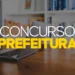 Notebook aberto sobre mesa de madeira com estante de livros ao fundo e texto "Concurso Prefeitura" sobreposto