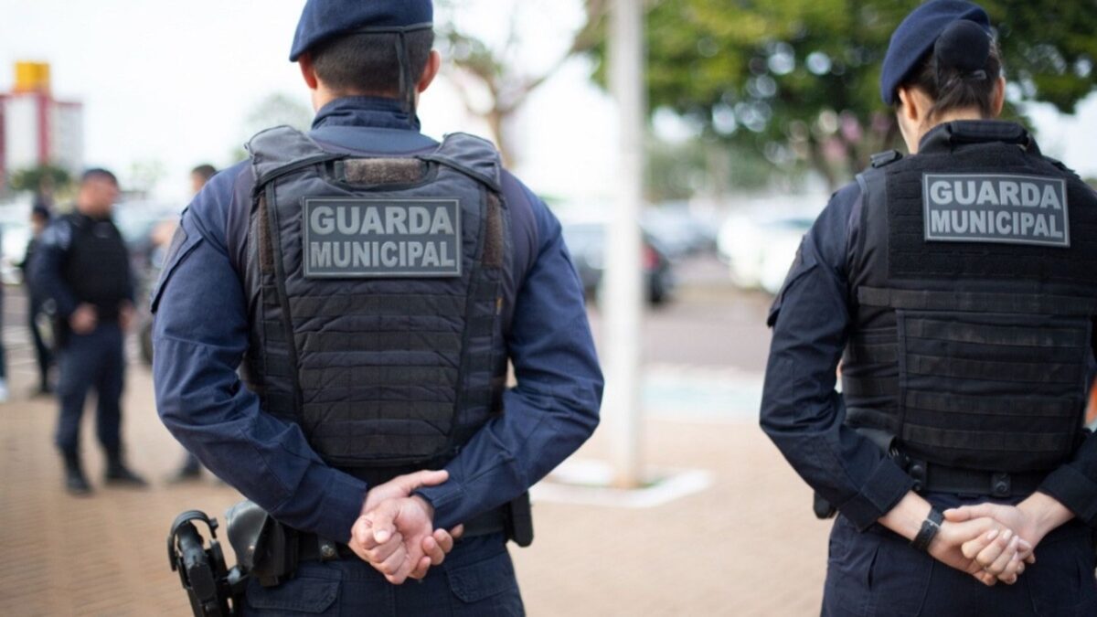 Concurso Guarda Municipal Dois agentes da Guarda Municipal patrulham uma área urbana ao ar livre em 2026