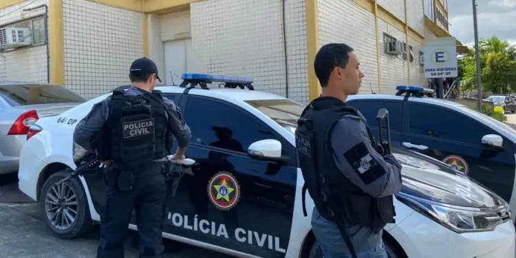 Dois policiais civis armados ao lado de uma viatura com a identificação da Polícia Civil