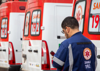 Linha de ambulâncias SAMU 192 com profissional de saúde usando uniforme azul observando celular