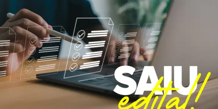 Pessoa usando um laptop enquanto edita documentos, com várias folhas de papel ilustradas com marcação de verificação. A imagem simboliza o lançamento de um edital para concurso público.