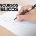 Pessoa preenchendo uma folha de questões de concurso público com uma caneta preta, em um ambiente.