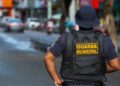 Agente da Guarda Municipal de costas, patrulhando uma rua movimentada em 2026