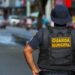 Agente da Guarda Municipal de costas, patrulhando uma rua movimentada em 2026