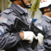 Policiais militares de São Paulo em uniforme cinza com capacete e armamento segurando arma de fogo preta