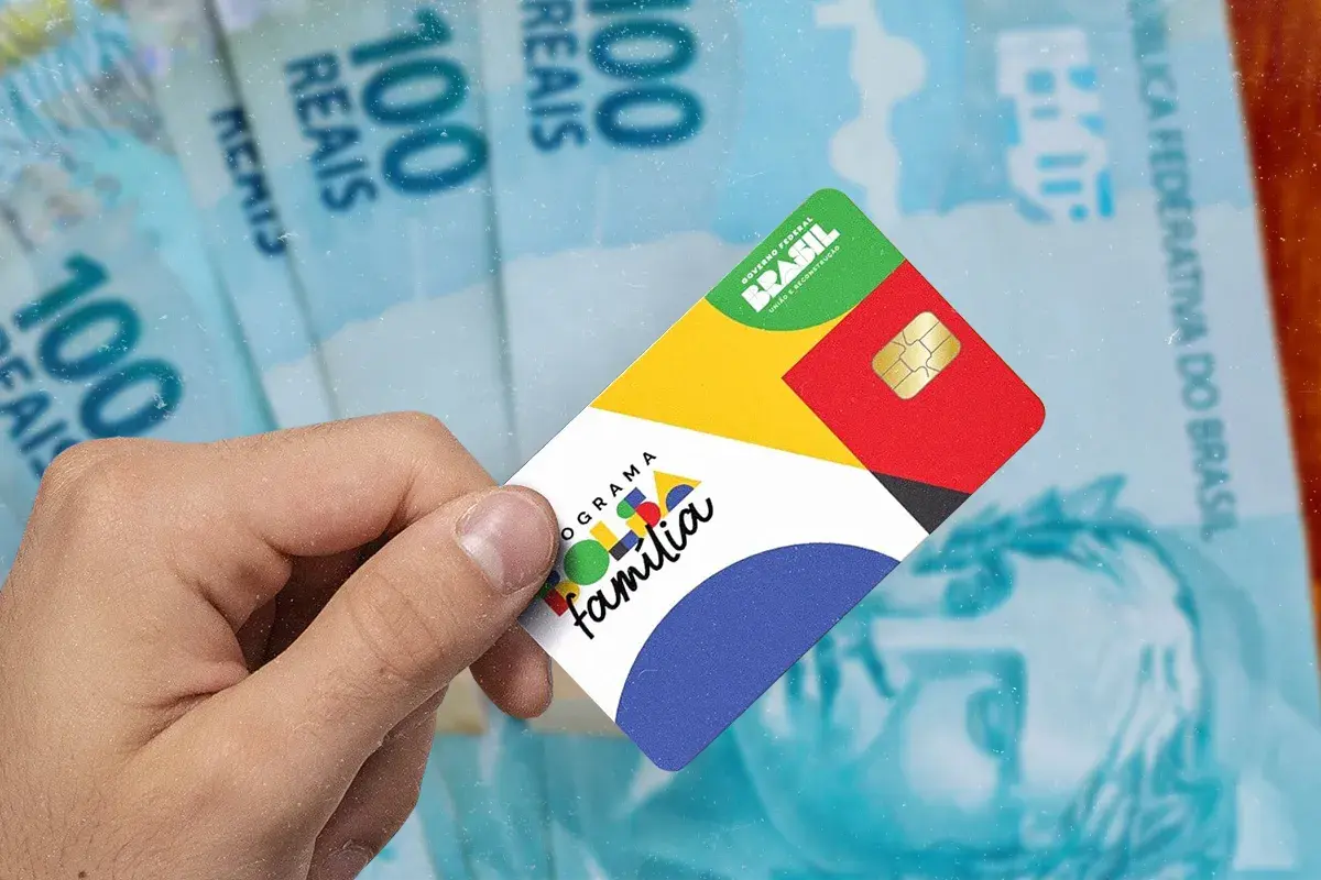 Recurso sobre frequência escolar no Bolsa Família. Cartão do Programa Bolsa Família sendo segurado por uma pessoa, com cédulas de 100 reais ao fundo, representando o benefício financeiro.