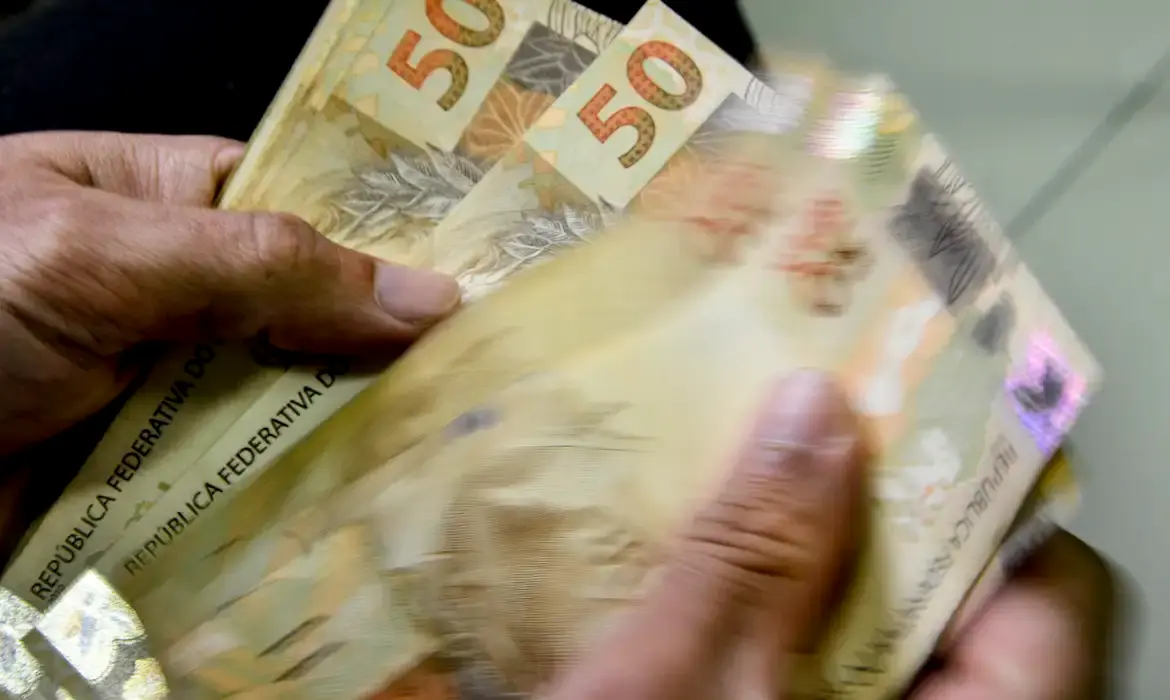 Modalidade de Crédito Especial Imagem mostrando uma pessoa manuseando notas de 50 reais, representando o crédito especial disponível para trabalhadores com carteira assinada.