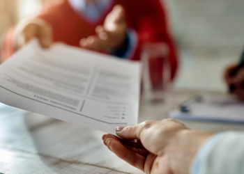 Mão entregando um currículo impresso durante uma entrevista de emprego