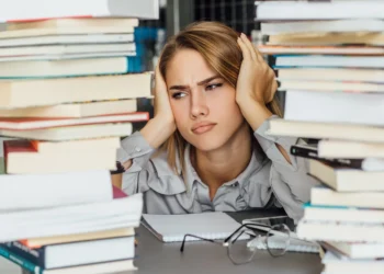 Mulher frustrada com pilha de livros, pensando sobre por onde começar a estudar para o concurso público.