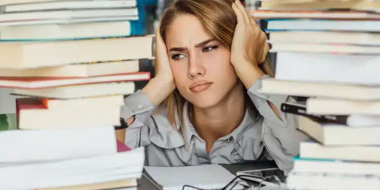 Mulher frustrada com pilha de livros, pensando sobre por onde começar a estudar para o concurso público.