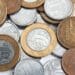 Diversas moedas do Plano Real espalhadas, incluindo moedas de 1 Real, 10 centavos e 25 centavos de diferentes anos; em evidência, uma moeda de 1 Real de 2008 com anel dourado e núcleo prateado.