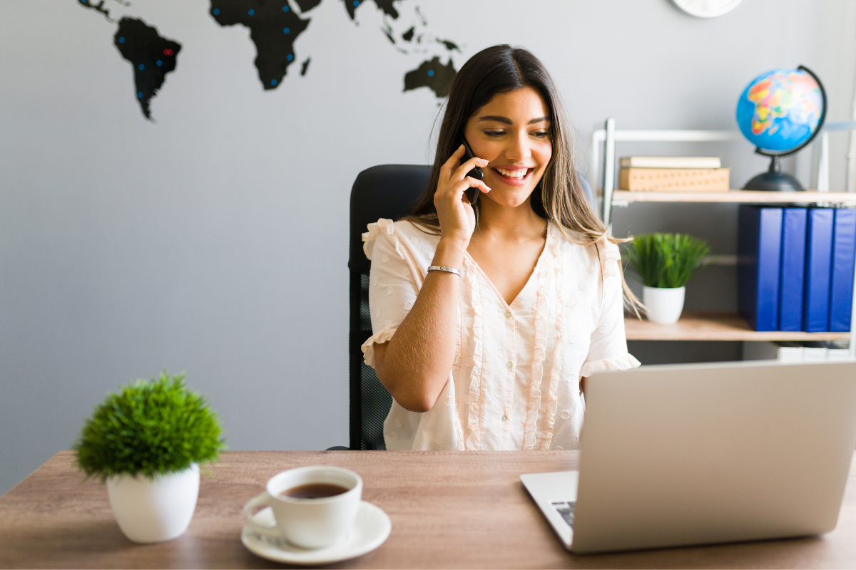 Diplomatas 2026 Mulher sorridente trabalhando em escritório, usando notebook e telefone