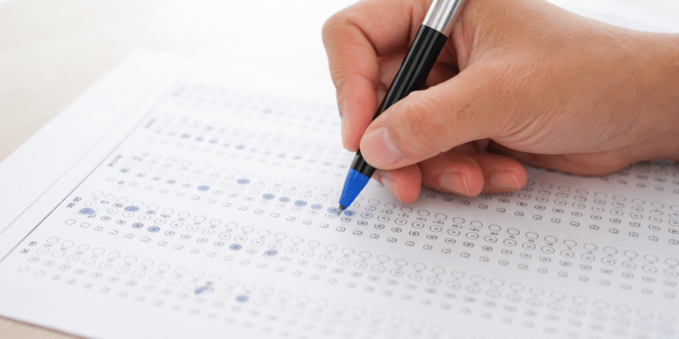 Pessoa preenchendo folha de respostas de múltipla escolha com caneta, representando concurso.