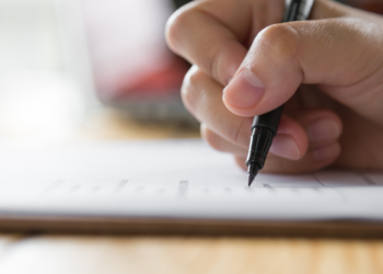 Mão segurando uma caneta preta enquanto faz anotações em papel
