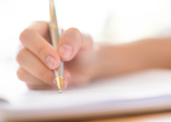 Pessoa segurando caneta dourada enquanto escreve em folha de papel