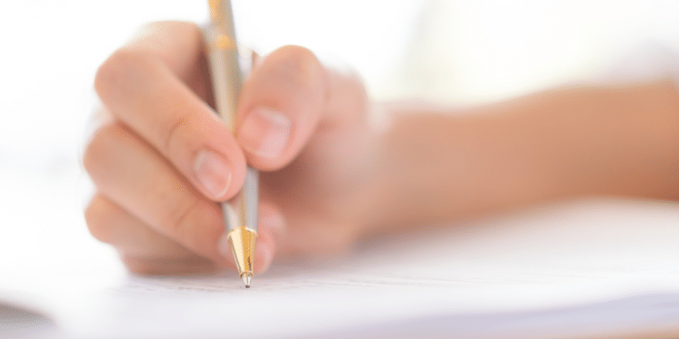 Pessoa segurando caneta dourada enquanto escreve em folha de papel