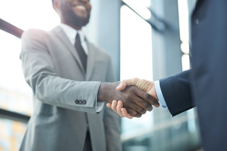 Entrevista de emprego: feedbacks. Profissional apertando a mão de outro em um ambiente de escritório moderno.