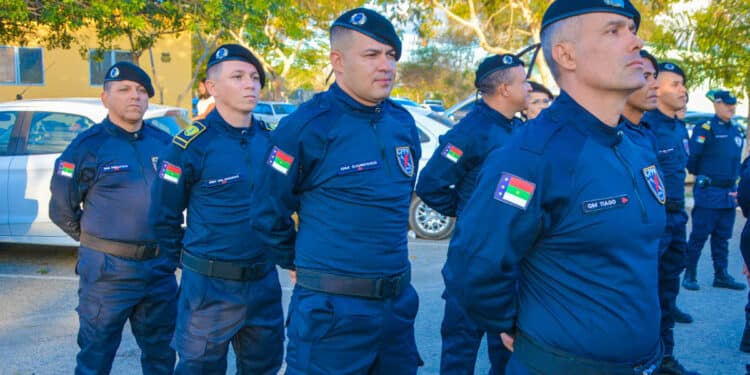 Grupo de guardas municipais alinhados em formação usando uniforme azul e boina preta em área externa.