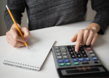 Mãos usando lápis para anotar números e calculadora para fazer cálculos sobre mesa branca