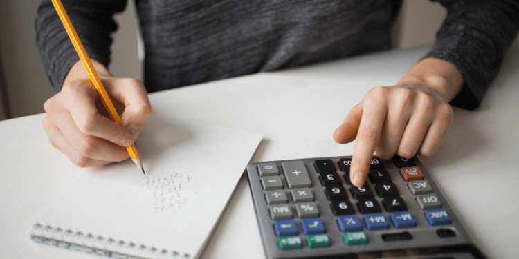 Mãos usando lápis para anotar números e calculadora para fazer cálculos sobre mesa branca