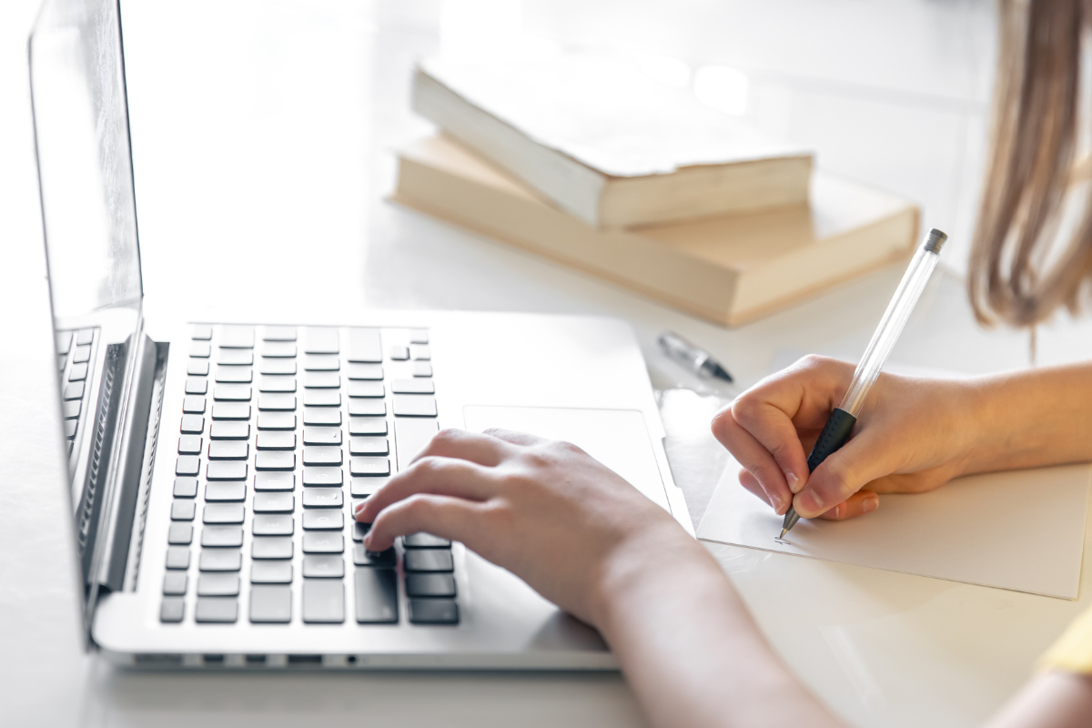 Inscrição Prefeitura Jundiaí SP Pessoa usando notebook enquanto faz anotações manuais com livros ao fundo