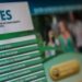 Tela de monitor exibindo o portal oficial do FIES (Programa de Financiamento Estudantil). Em destaque, um menu lateral verde com opções como "O que é o Fies?", "Como se inscrever", "Condições de financiamento" e "Perguntas frequentes". Ao fundo, uma imagem desfocada de jovens em um ambiente universitário.