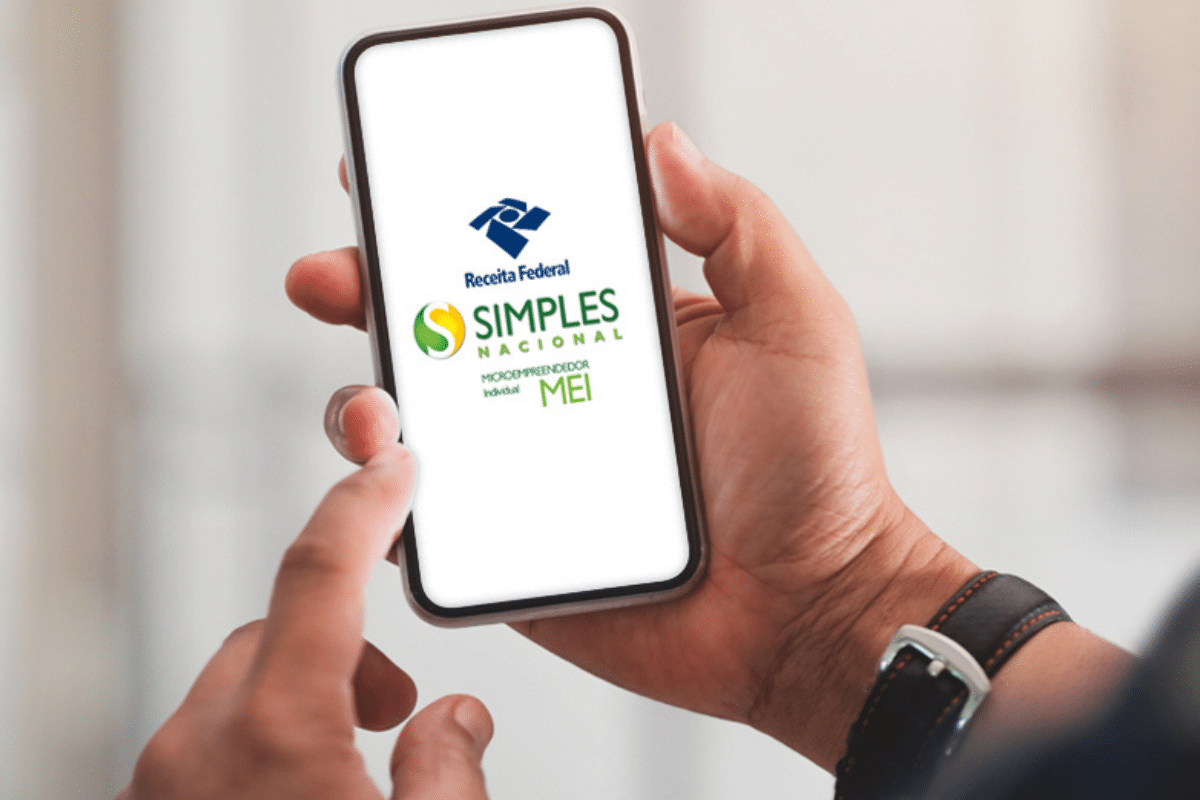 Lista profissões proibidas MEI 2026 Mão segurando celular com tela mostrando logo da Receita Federal, Simples Nacional e MEI.