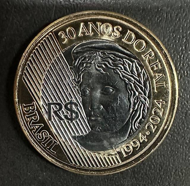 detalhe design moeda comemorativa 2024 Close-up em alta definição do anverso da moeda de 30 anos do Real, destacando o brilho do aço inox e as linhas diagonais do fundo.
