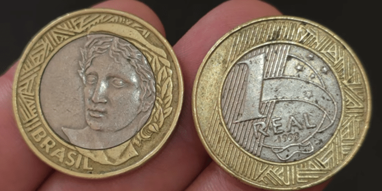 Duas moedas de 1 real de 1998 lado a lado; a da esquerda mostra o anverso com a efígie da República e a da direita exibe o valor de face, o ano 1998 e o núcleo prateado.