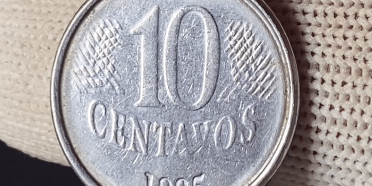 Close detalhado de diversas moedas brasileiras de um real e de centavos empilhadas sobre uma mesa de madeira, com foco em uma moeda de um real em destaque.