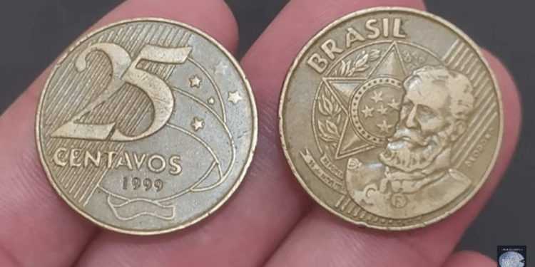 Duas moedas de 25 centavos de 1999 sendo seguradas, mostrando as faces anverso (busto de Deodoro) e reverso (valor "25 centavos").