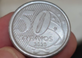 Fotografia em close-up do reverso de uma moeda de 50 centavos de 2020, segurada entre os dedos. A imagem destaca o número 50, a palavra "CENTAVOS" e o ano de fabricação 2020 sobre o fundo de linhas diagonais.