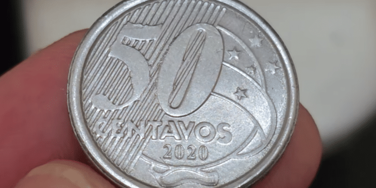 Fotografia em close-up do reverso de uma moeda de 50 centavos de 2020, segurada entre os dedos. A imagem destaca o número 50, a palavra "CENTAVOS" e o ano de fabricação 2020 sobre o fundo de linhas diagonais.