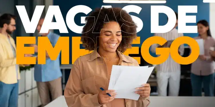 Mulher negra sorridente em primeiro plano segurando currículos em um escritório, com o texto "VAGAS DE EMPREGO" sobreposto em letras grandes brancas e laranjas. Ao fundo, outros profissionais desfocados conversam.