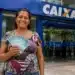 Mulher segurando cédulas de dinheiro brasileiro em frente a uma agência da Caixa representando os pagamentos do Bolsa Família de julho.