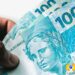 Notas de R$100 do Brasil sendo seguradas, representando o valor do Pix a ser recebido em fevereiro pelo Pé-de-Meia.