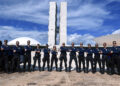 Grupo de agentes federais em uniforme azul posando com braços cruzados diante do Congresso Nacional do Brasil