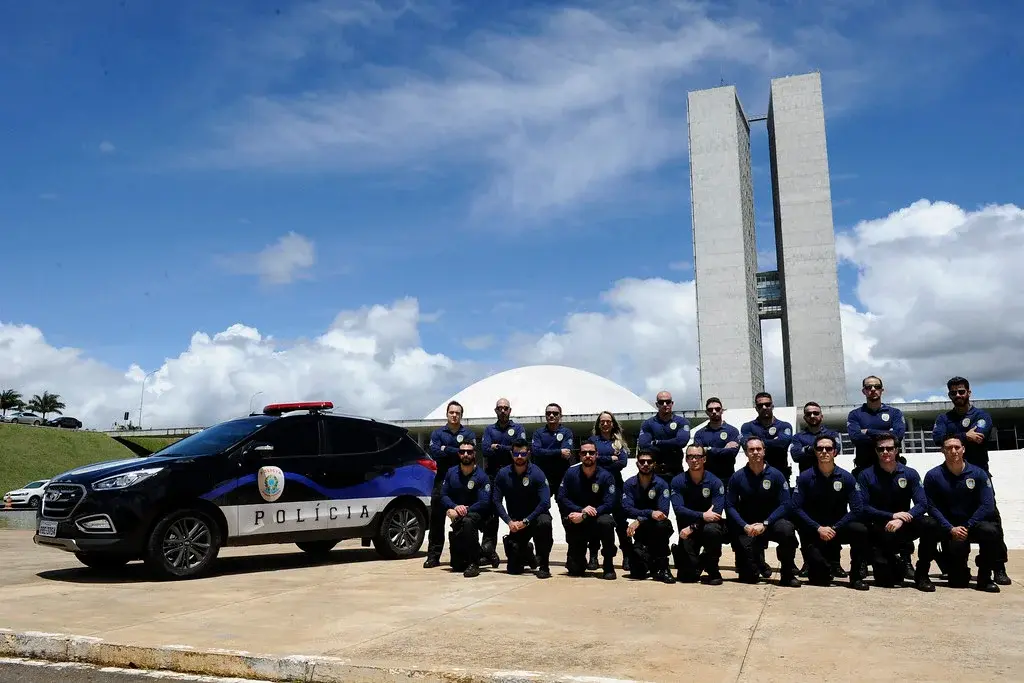 Concurso de Policial Legislativo Equipe de Policiais Legislativos em frente ao Congresso Nacional, com um veículo oficial e o icônico edifício ao fundo.