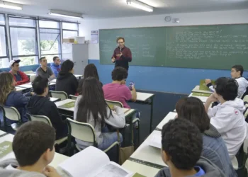 Professor ensina alunos em sala de aula com lousa e carteiras organizadas, educação escolar em 2026
