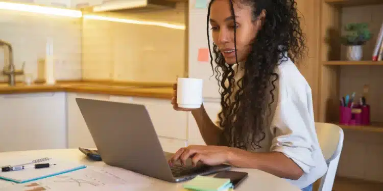 Profissional trabalhando de casa, analisando gráficos e tomando café em um ambiente doméstico com laptop.