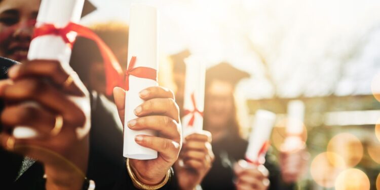Formandos segurando seus diplomas, representando a conquista da educação superior, mas também refletindo as dificuldades no mercado de trabalho.