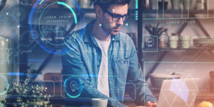 Homem jovem de óculos e camisa jeans trabalhando em um notebook, cercado por interfaces digitais holográficas azuis que exibem gráficos, dados e ícones de tecnologia.