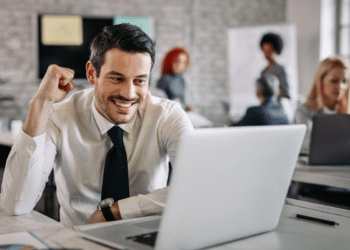 Homem sorrindo satisfeito em frente ao notebook, comemorando resultado positivo no trabalho