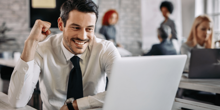 Homem sorrindo satisfeito em frente ao notebook, comemorando resultado positivo no trabalho
