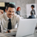 Homem sorrindo satisfeito em frente ao notebook, comemorando resultado positivo no trabalho