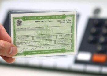 Mão segurando um título eleitoral brasileiro com detalhes de identificação biométrica e informações pessoais.