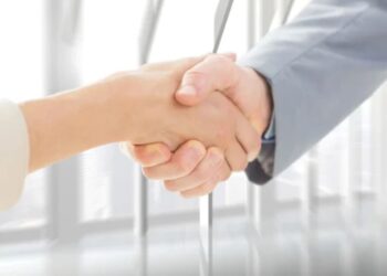 Aperto de mão entre duas pessoas em um ambiente profissional, simbolizando uma conexão ou acordo.