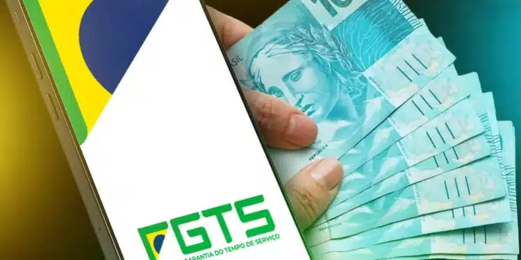 Imagem mostrando a tela de um celular com o logo do FGTS, junto a uma mão segurando várias cédulas de 100 reais, ilustrando o Saque-aniversário 2026.