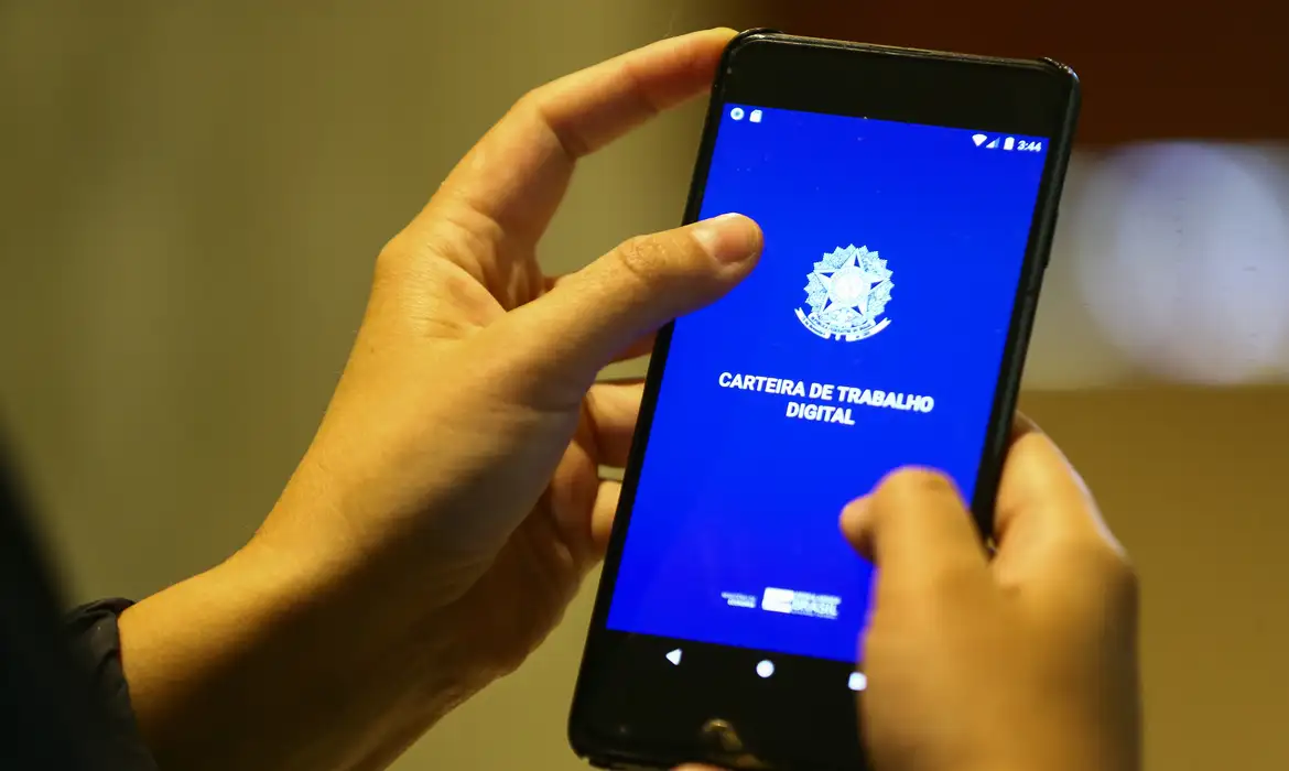 Solicitação Seguro-Desemprego 2026 Pessoa segurando smartphone com a tela mostrando a Carteira de Trabalho Digital em azul