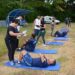 Pessoas realizando exercícios abdominais em colchonetes, sendo avaliadas por instrutores ao ar livre em 2026